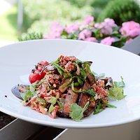 Gegrillte schweinenackensteaks auf marinierten auberginen mit tomaten-oliven-tapenade, gegrillten zuckerschoten und frischem koriander