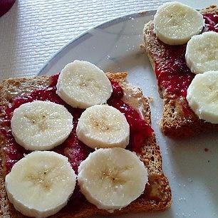 Gesunde frühstücksidee mit vollkorntoast, erdnussmus, cranberrymarmelade und banane